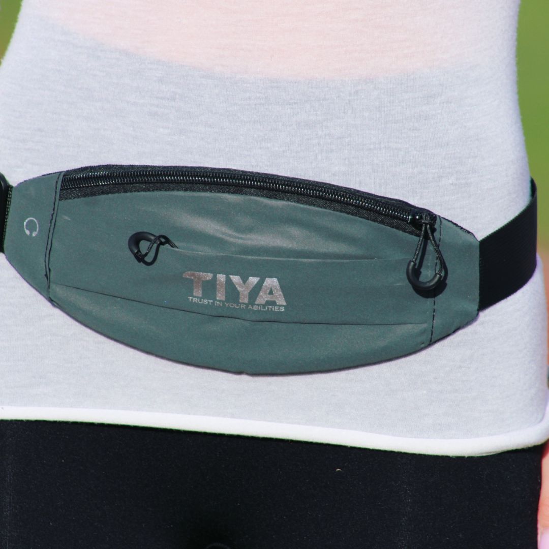 A person wearing the TIYA waist bag around the waist, showcasing its zippered front pocket.