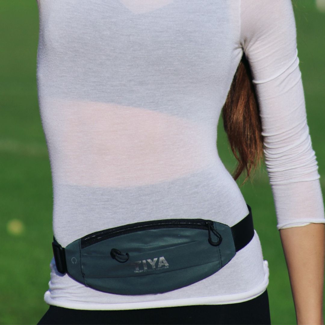 A person in athletic attire wearing the TIYA running belt for hands-free convenience during outdoor activities.